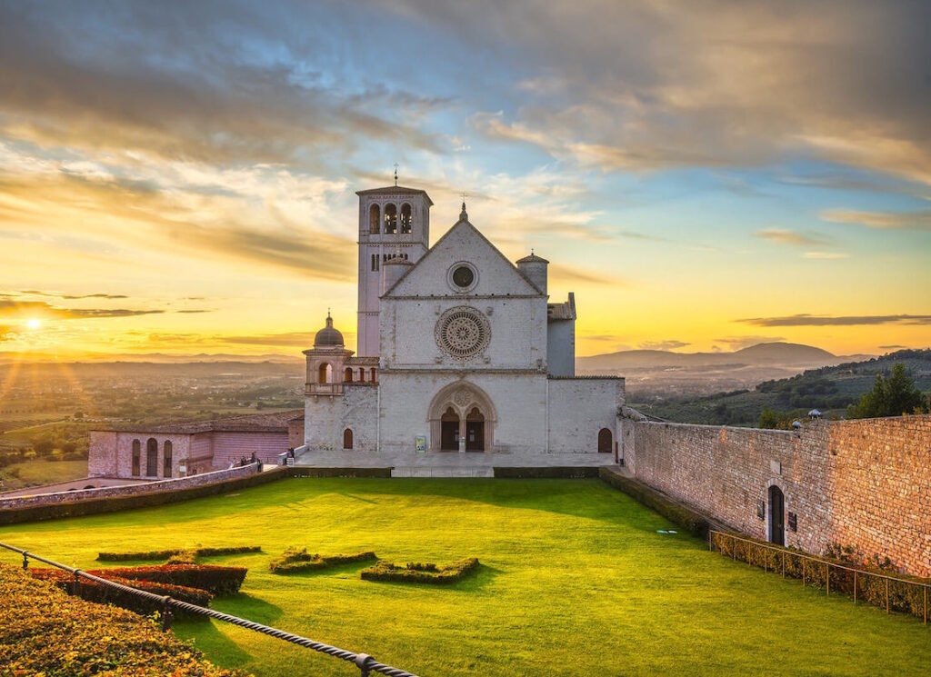 La facciata della basilica superiore di San Francesco ad Assisi con il rosone e il campanile, al tramonto