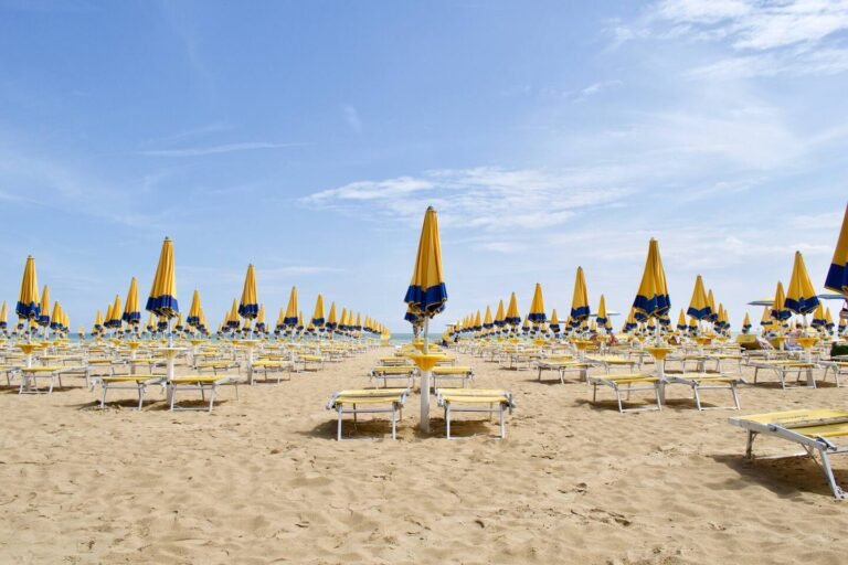 Spiaggia di Jesolo in coda d'estate: file di ombrelloni chiusi e sabbia quieta verso il mare