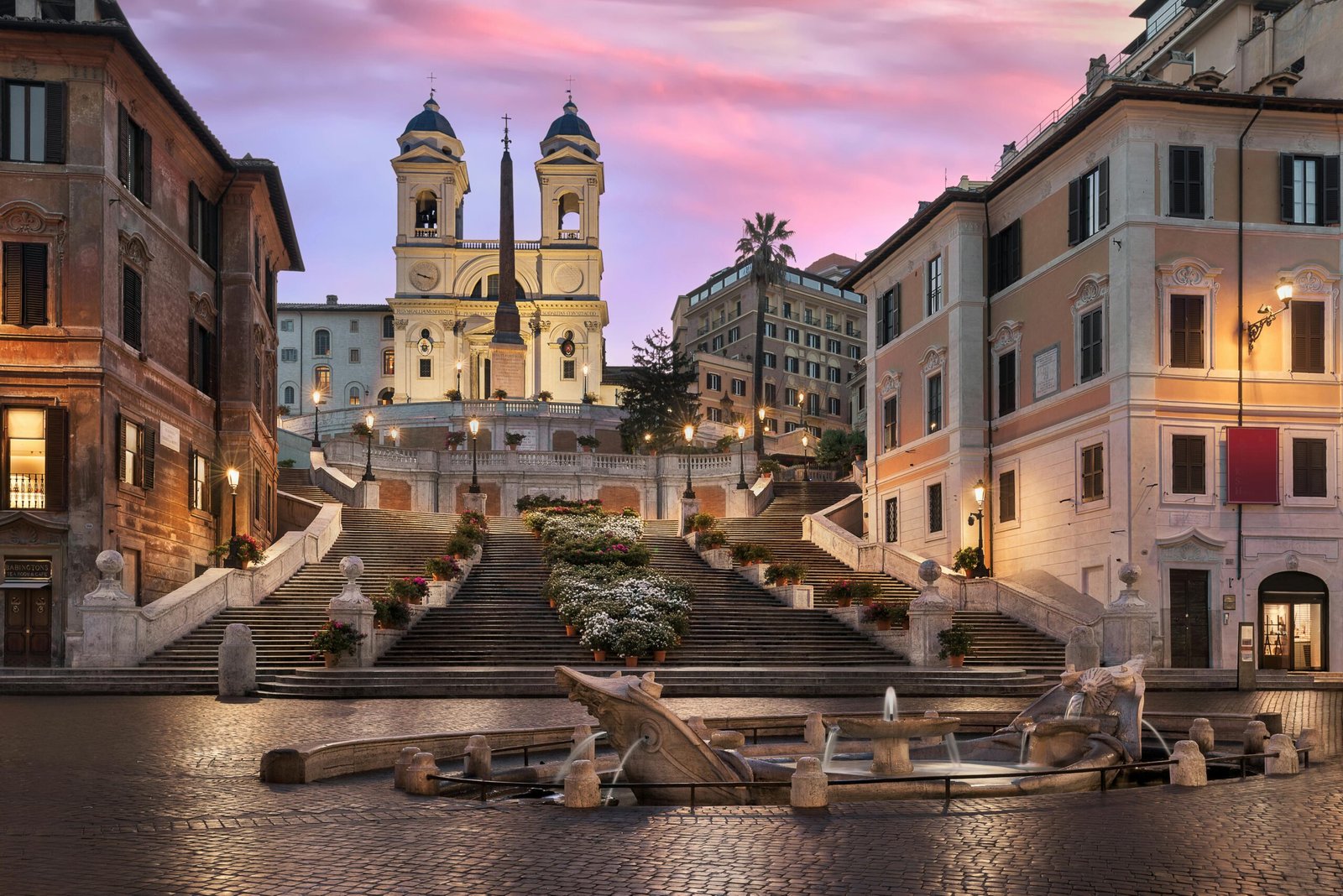 Piazza di Spagna a Roma al crepuscolo, con la Barcaccia, la scalinata e la chiesa di Trinità dei Monti sotto un cielo rosa