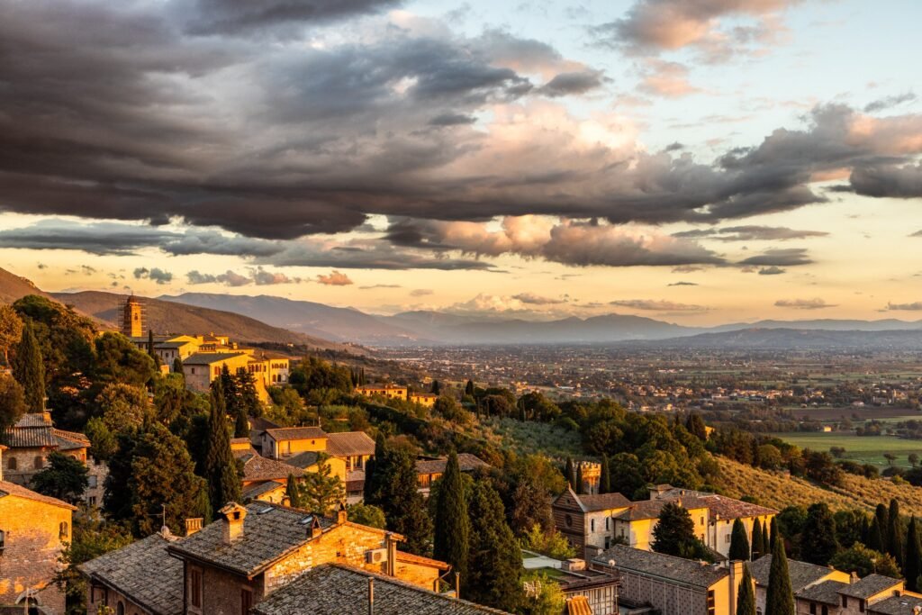 La Valle Umbra vista dai tetti di Assisi al tramonto d'autunno, con uliveti, cipressi e cielo carico di nuvole