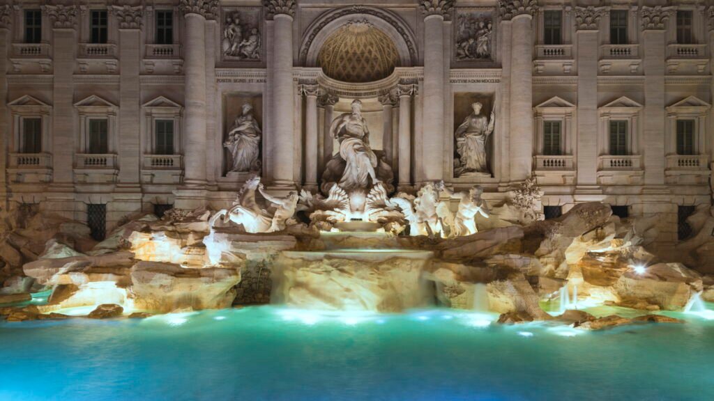 La Fontana di Trevi a Roma illuminata di sera, con l'acqua turchese e le statue barocche in luce calda