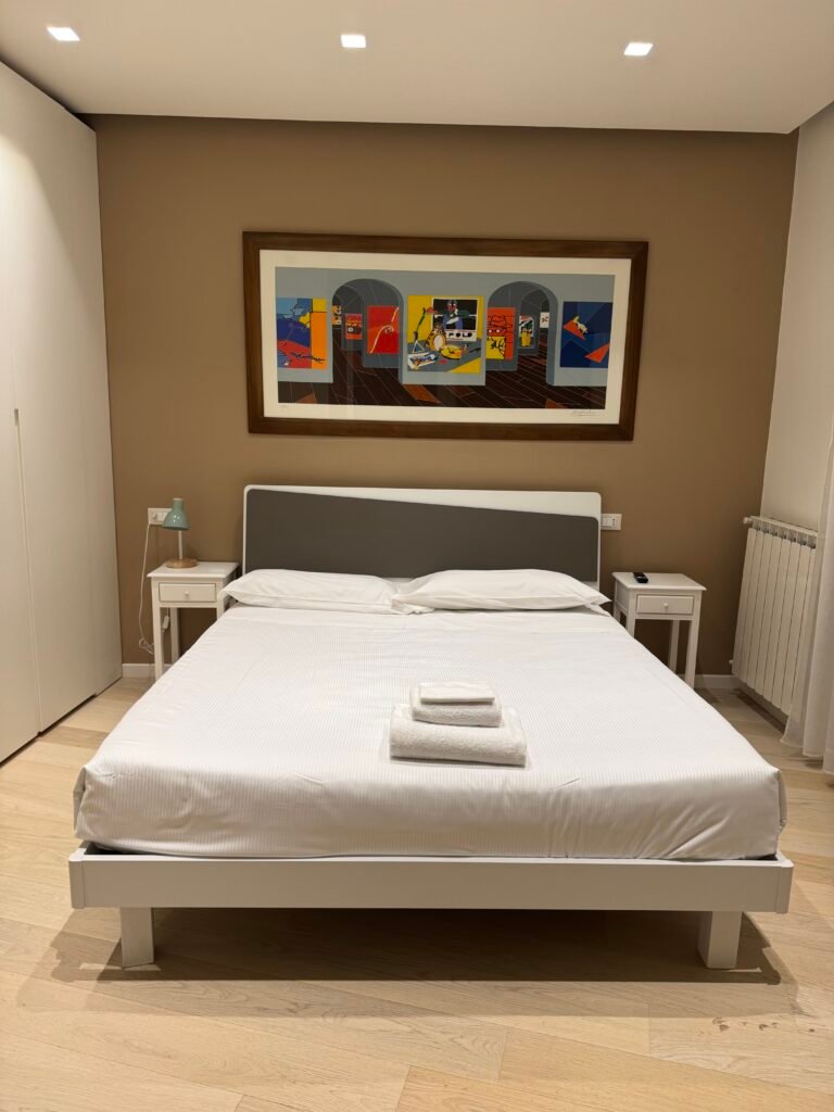 Camera matrimoniale dell'attico Luce ad Assisi con letto rifatto, asciugamani e quadro colorato alla parete