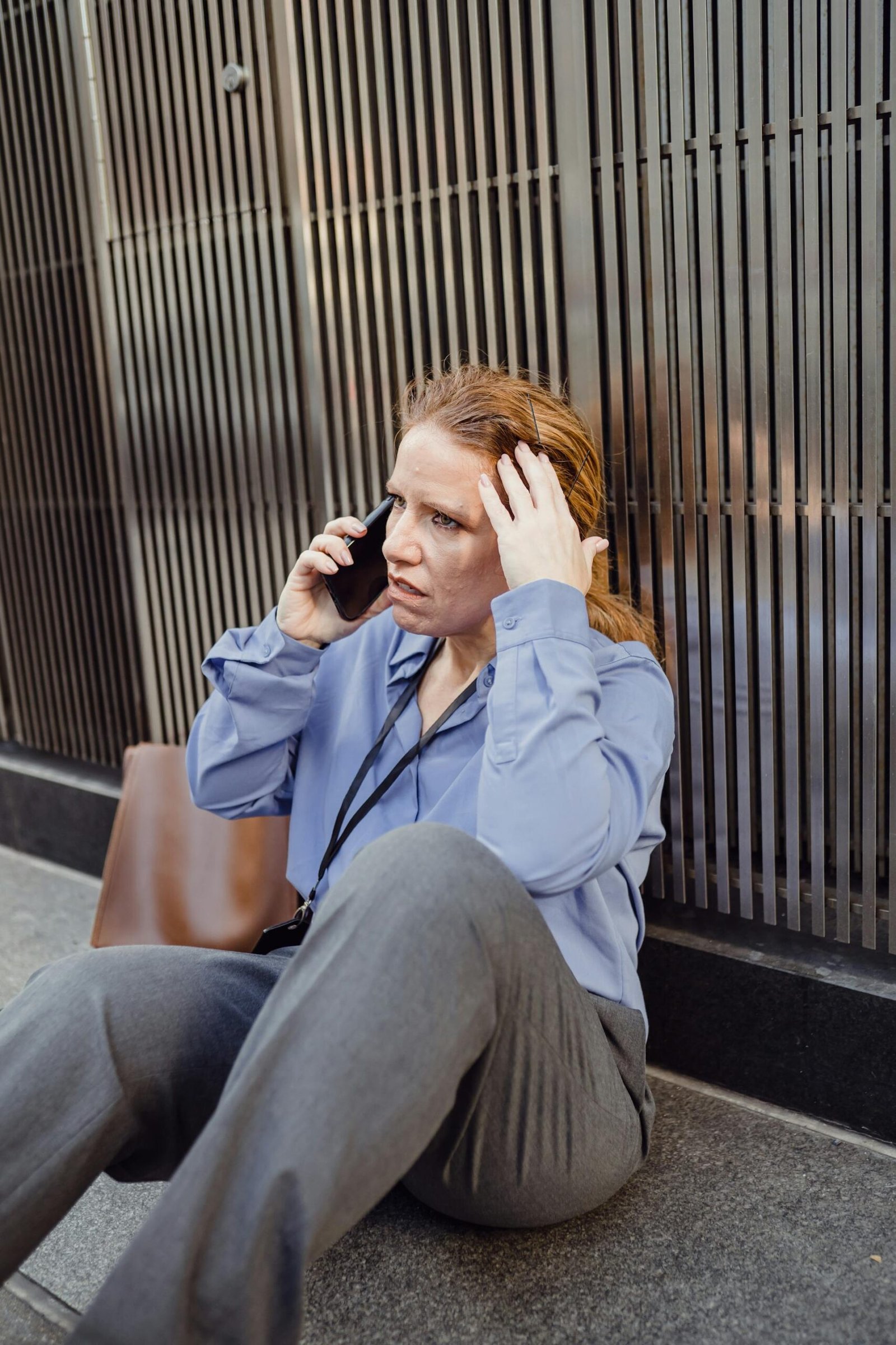 Una donna seduta sul marciapiede in una strada di città, telefono in mano, con espressione preoccupata