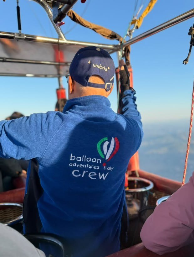 Membro dell'equipaggio di Balloon Adventures Italy visto di spalle nel cesto, con la valle sullo sfondo